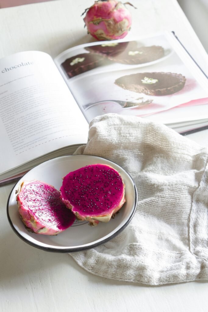 Sliced dragon fruit on a plate beside an open cookbook, showcasing vibrant colors.