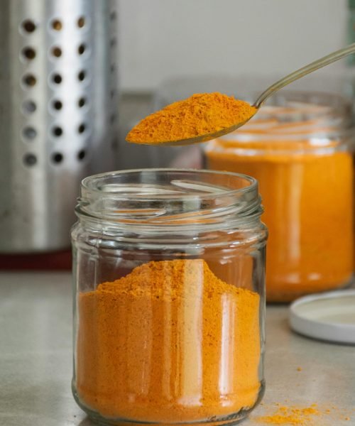 Close-up of bright turmeric powder in glass jars with spoon, enhancing culinary and health experiences.