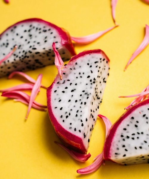 Sliced dragon fruit with pink petals on vibrant yellow tabletop.