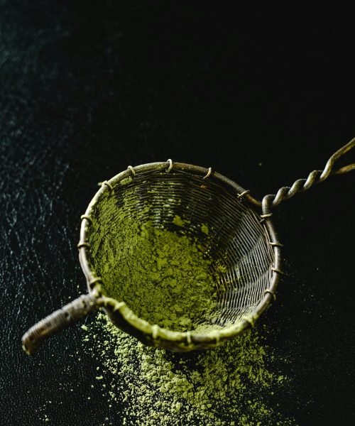 Green matcha powder in a bamboo sieve on a dark background, creating a natural texture.