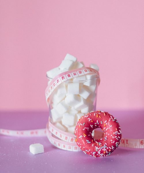 Pink donut with sugar cubes and tape measure on a pink surface.